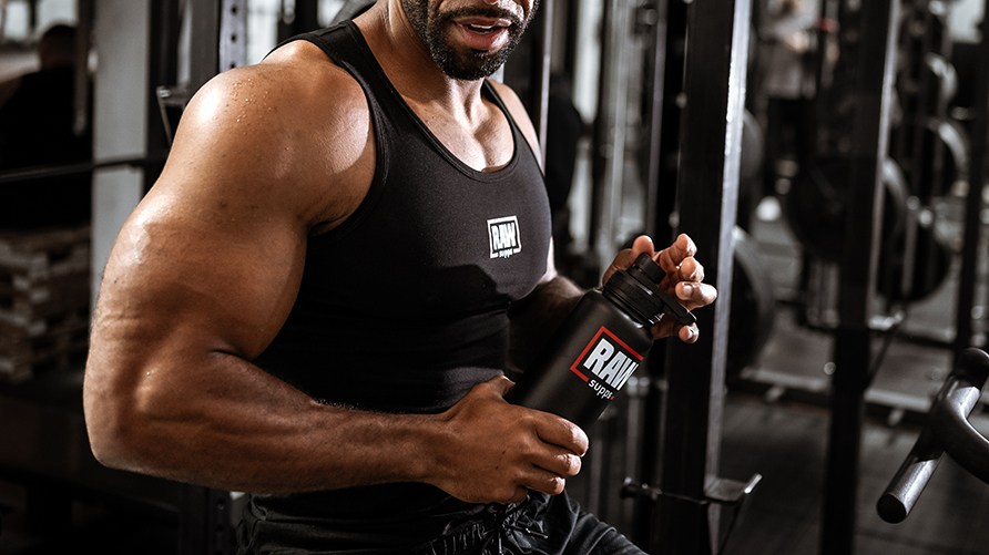 Henkil, jonka ylkroppa nkyy kuvassa, pitelee ksissn RAW Supps Insulated Sport Bottlea, plln RAW Supps toppi.